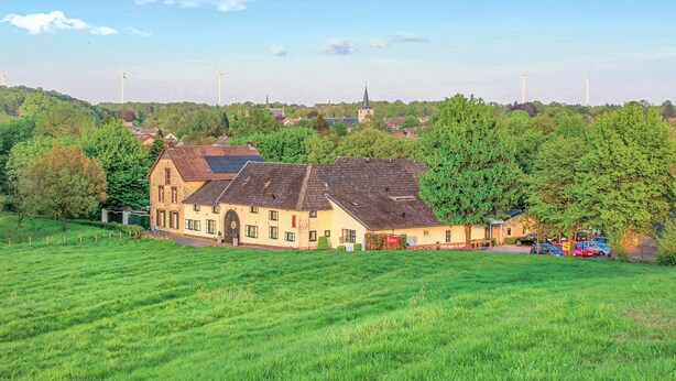 A rural building with a sloped roof, surrounded by green fields and trees.