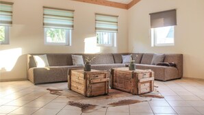 A living room with a large sectional sofa, two wooden crates as side tables, and a cowhide rug on a tiled floor. - Amazing apartment in Simpelveld (Simpelveld)
