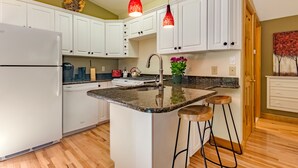 A kitchen with white cabinets, a granite countertop, a stainless steel sink, and a red pendant light.