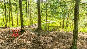 A hammock in a forest with a red stool nearby.