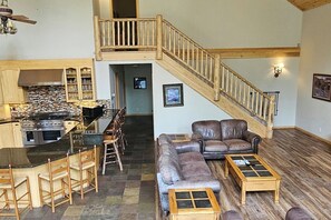A spacious living area with a wooden staircase, a leather sofa, and a kitchen with a bar.