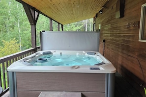 Un jacuzzi en una terraza de madera con vista a árboles.