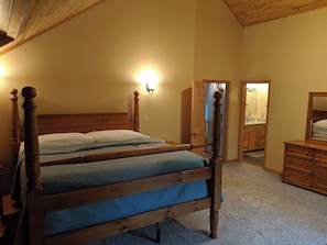 A bedroom with a wooden four-poster bed, a nightstand, a dresser, and a mirror.