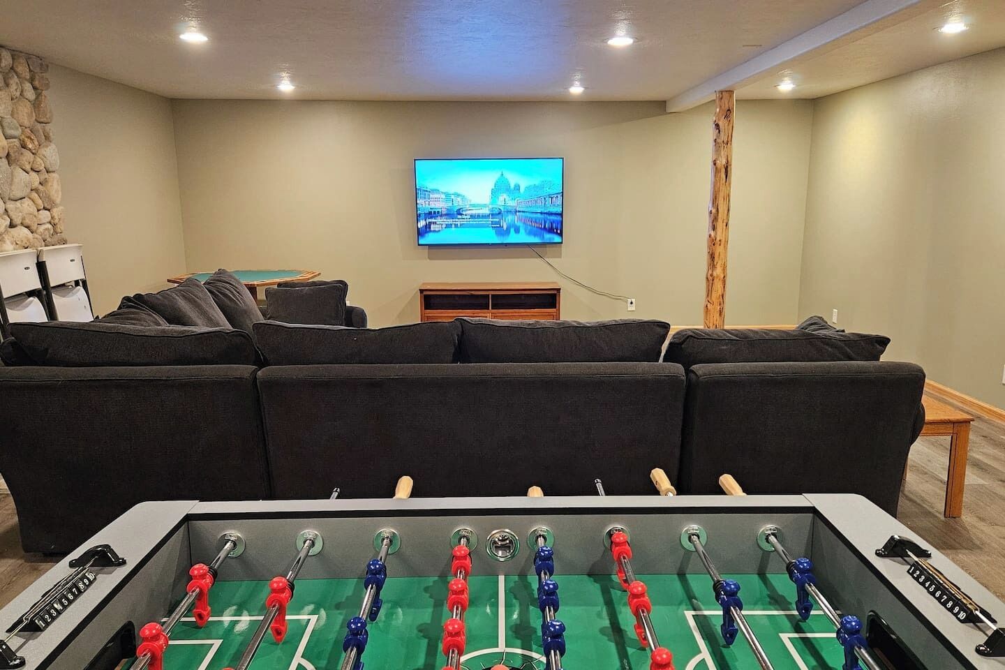 A living room with a foosball table, a sofa, a television, and a stone wall.