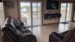 A living room with a leather sofa, a television, and a sliding glass door leading to an outdoor patio. - "Canal-Front Paradise in Big Pine Key-Relax &Explore the keys" (Big Pine Key)