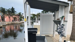 A covered outdoor area with a concrete floor, a white fence, and a water body in the background. - "Canal-Front Paradise in Big Pine Key-Relax &Explore the keys" (Big Pine Key)
