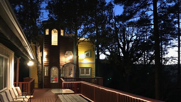 Une terrasse en bois avec des tables et des chaises pour pique-nique, un petit bâtiment doté de fenêtres en arc de cercle et une rambarde.