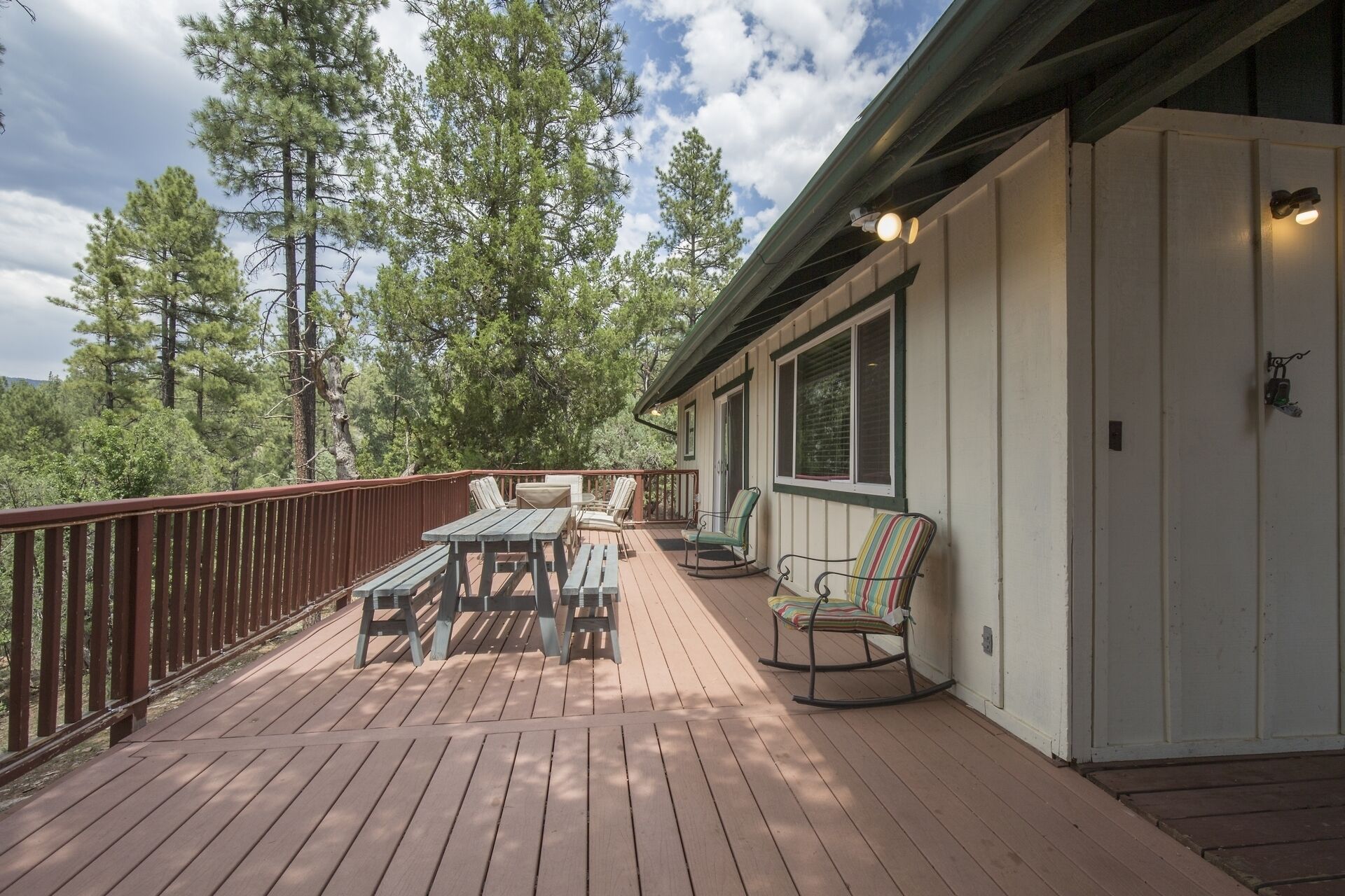 A wooden deck with a table and chairs, a rocking chair, and a door with a light fixture.
