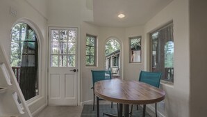 Un coin repas avec une table ronde et deux chaises, une porte blanche et de grandes fenêtres donnant sur la forêt.
