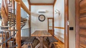 Ein rustikales Holzinnere mit einem zentralen Holztisch und Bänken, einer Wendeltreppe und einer an der Wand befestigten Uhr.