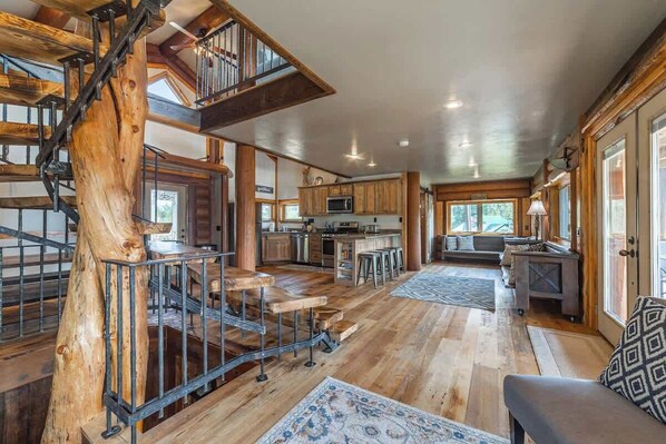 Un interior amplio con una escalera de madera, una zona de cocina y una sala de estar con un tapete estampado.