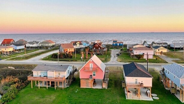 A coastal residential area with houses on stilts, a clear view of the ocean, and a road in the foreground. - King size bed! Freeport Surfside Beach Bungalow Ocean & BayViews,Steps from Ocea (Surfside Beach)