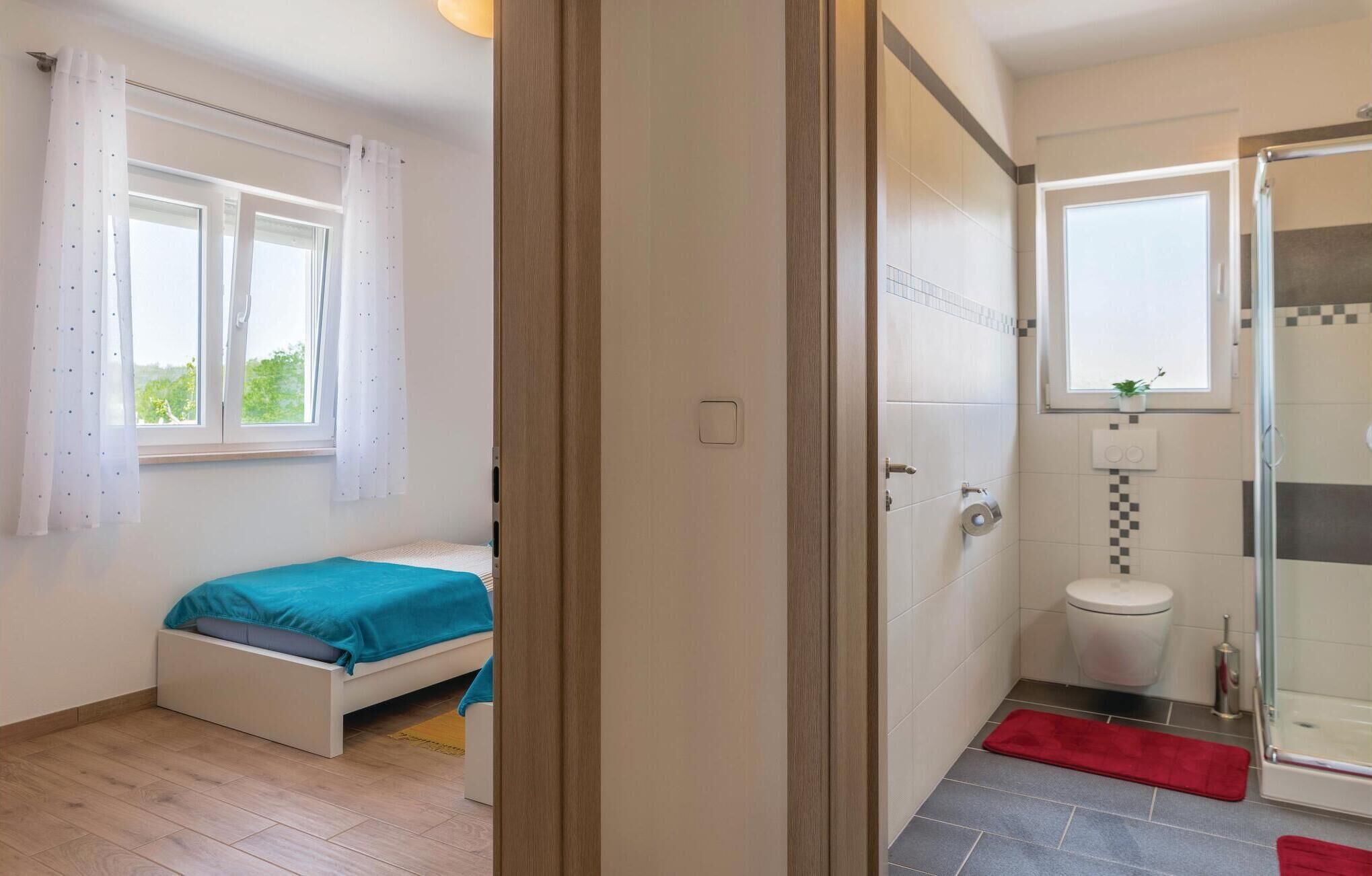 A bedroom with a bed, a bathroom with a toilet and shower, and a window with curtains.