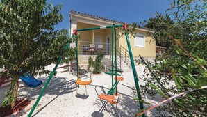 A playground with swings and a climbing structure in front of a house with a balcony. - Nice home in Liznjan with WiFi (Liznjan)