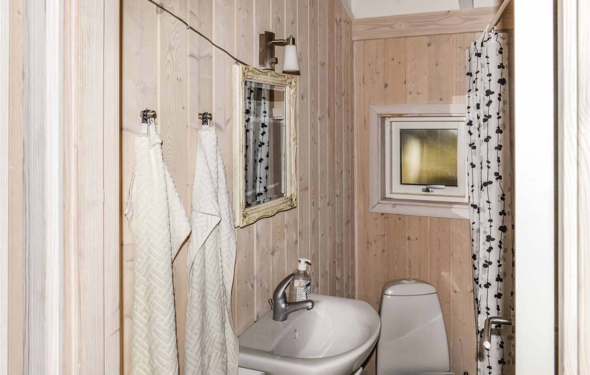 Un baño con paneles de madera, un lavamanos blanco, un espejo y un inodoro.