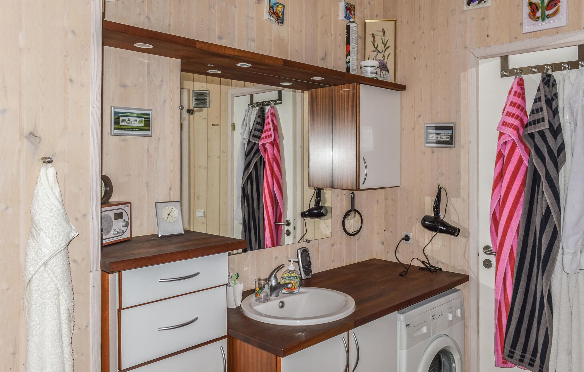 Een badkamer met houten paneelwanden, een grote spiegel, een wastafel, een wasmachine en handdoeken die aan de muur hangen.