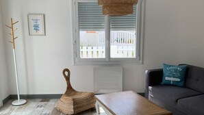 Ein Wohnzimmer mit Couchtisch aus Holz, einem Korbstuhl, einem grauen Sofa und einer Stehlampe.