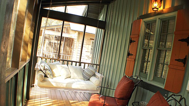 A porch with a white sofa, orange chairs, and a wooden table. - Romantic Spa Experience in Luxurious Creekside Honeymoon Cottage in the Landings (Steinhatchee)