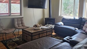 A cozy living room with a fireplace, a flat-screen TV, comfortable seating, and a view of trees through the windows. - Cabin in bass lake vacational (Wishon)