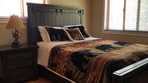 A bedroom with a bed, a nightstand, a lamp, a window with blinds, and a headboard. - Cabin in bass lake vacational (Wishon)