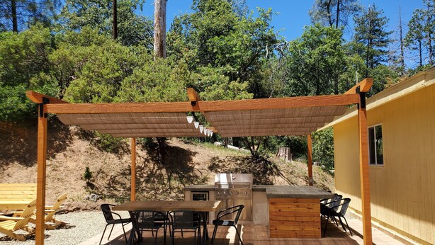 An outdoor patio with a wooden pergola, a table with chairs, and a built-in grill. - Cabin in bass lake vacational (Wishon)