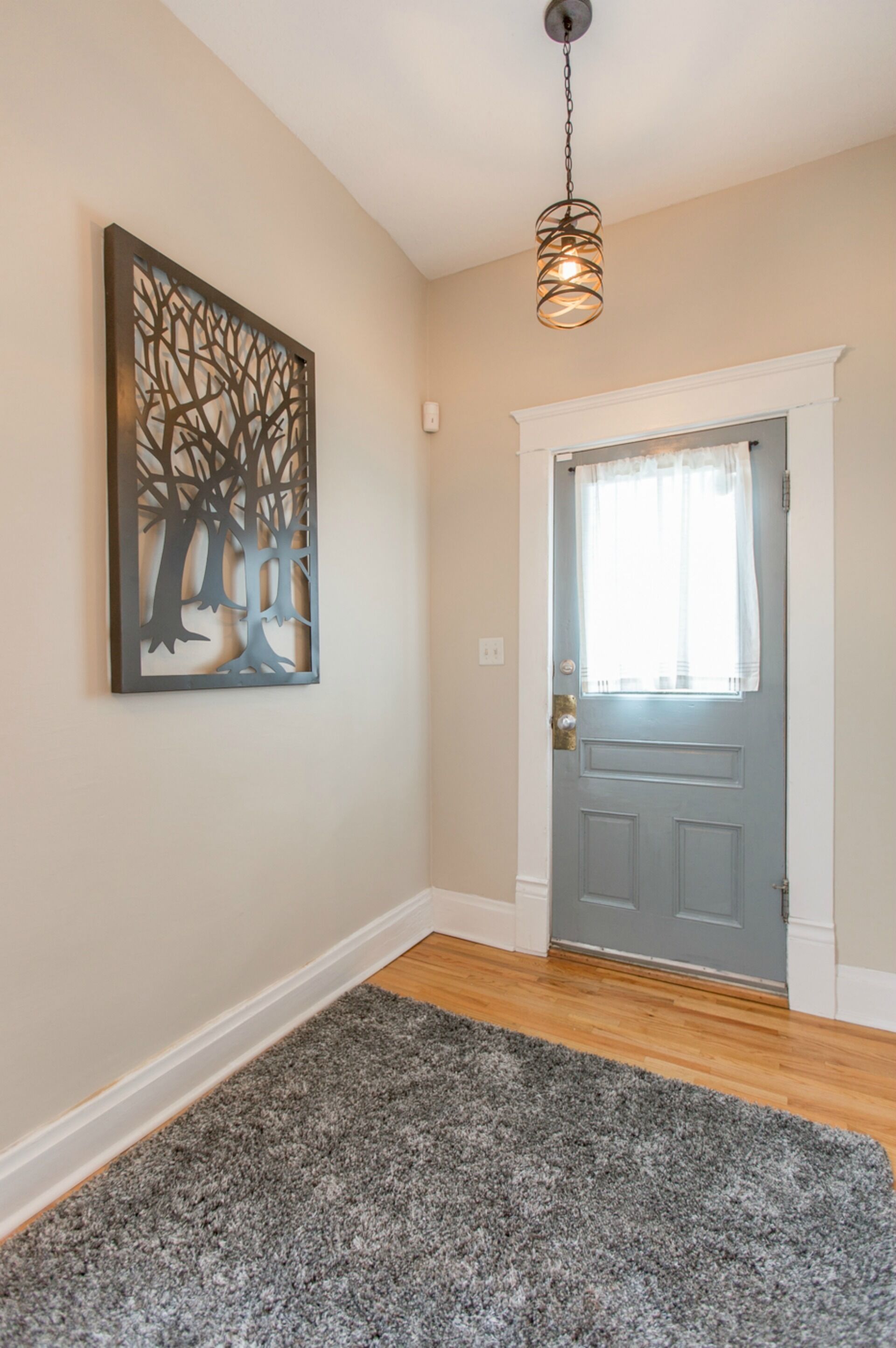 A hallway with a gray carpet, a gray door with a white trim, and a wall-mounted artwork depicting trees.