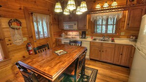A wooden cabin interior with a dining table, chairs, a kitchen area with a stove, microwave, and sink, and a refrigerator. - Bears Den, Pigeon Forge, Arcade game, Hot Tub (Pigeon Forge)