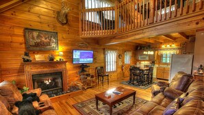 A cozy log cabin interior with a fireplace, leather sofas, a dining area, and a kitchen. - Bears Den, Pigeon Forge, Arcade game, Hot Tub (Pigeon Forge)
