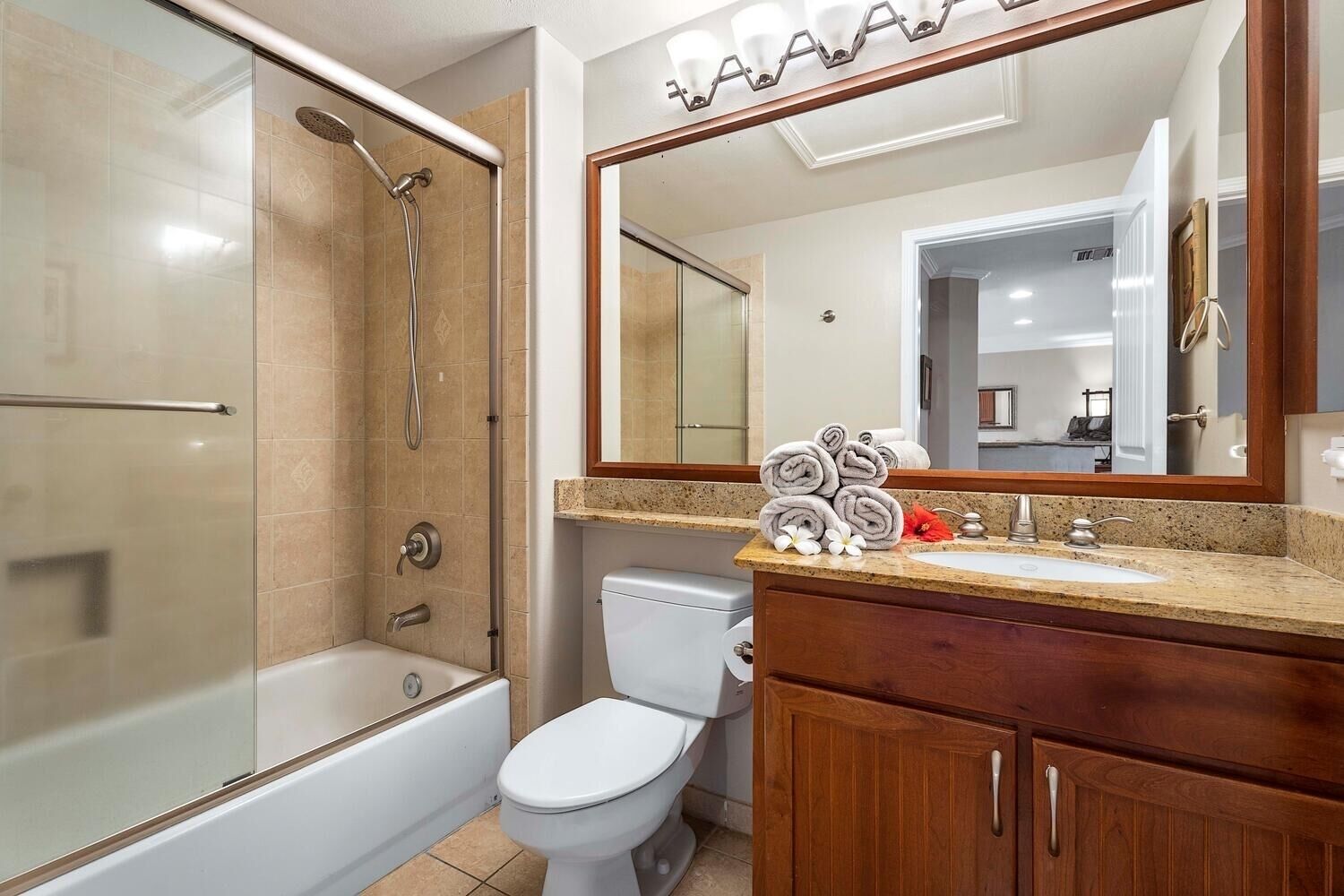 A bathroom with a glass-enclosed shower, a toilet, a sink with a mirror above it, and a wooden vanity.