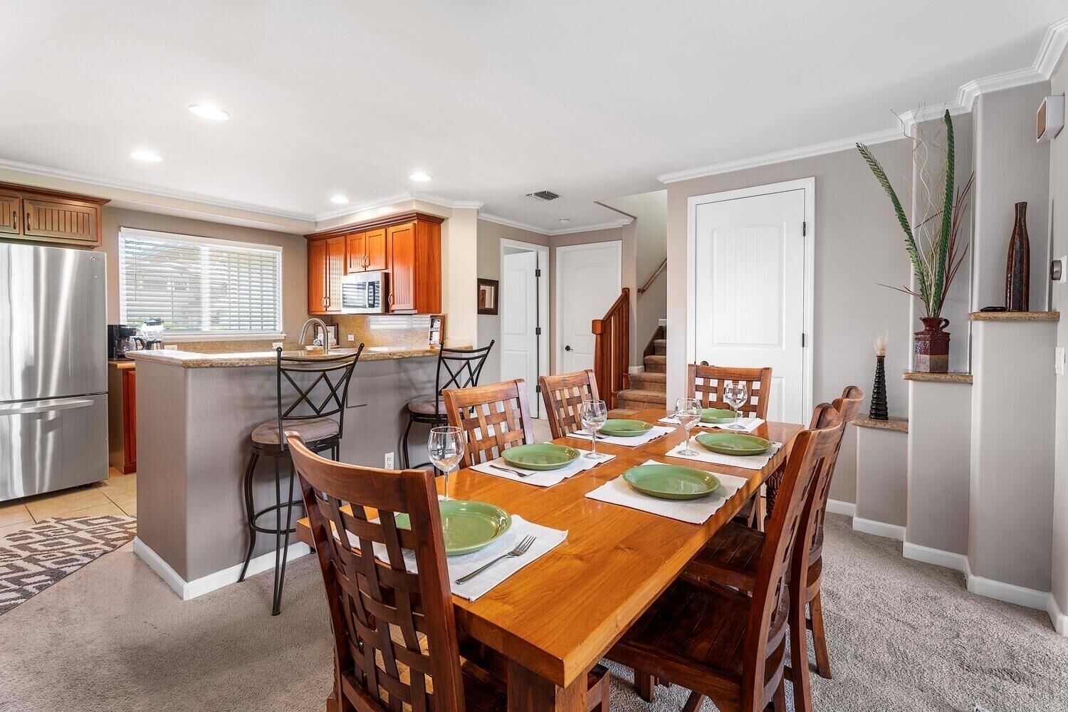 Une cuisine moderne dotée d’un îlot central, d’une table à manger en bois avec des chaises, et d’un escalier menant à un autre niveau.