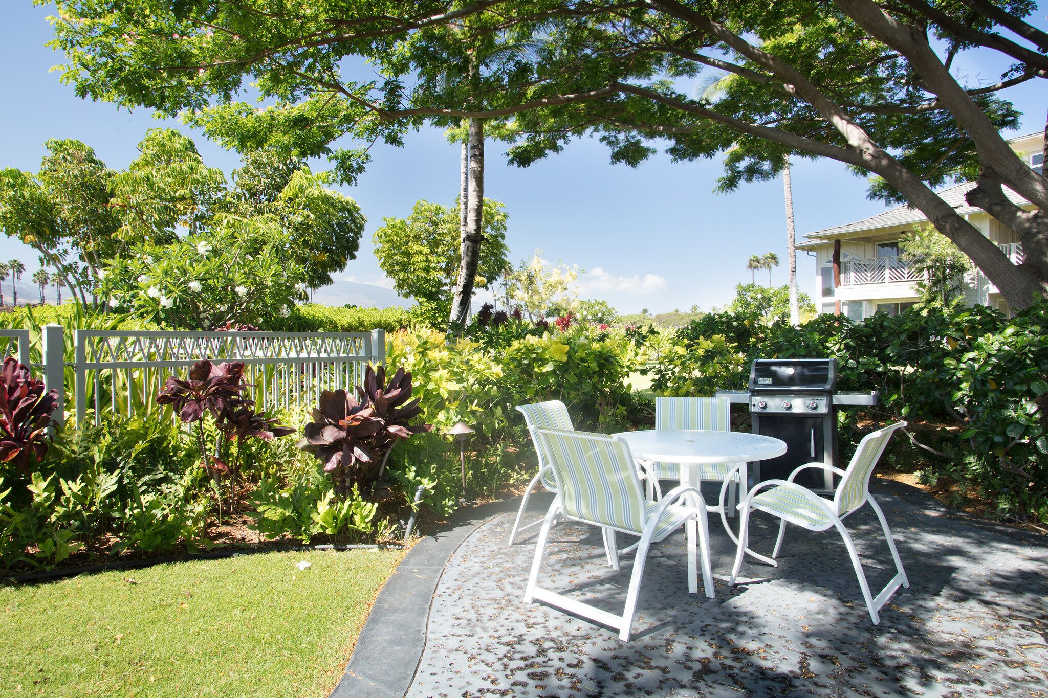 Eine Terrasse im Freien mit Grill, weißen Stühlen und üppiger Bepflanzung.
