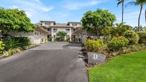 A residential building with a driveway leading to a gated entrance, surrounded by lush greenery and palm trees. - 2026 Waikoloa Hilton pool pass included 6 guests daily, available through 2026! (Waikoloa Village)