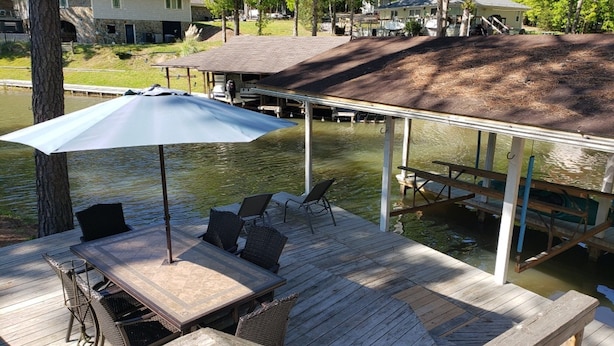 A wooden deck with a table and chairs, an umbrella, and a view of a lake. - Beautiful Waterfront Home on Lake Gaston + Pontoon Rental Option (Henrico)