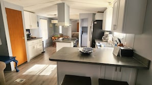 A modern kitchen with a central island, two bar stools, and a dining area with a table and chairs. - Beautiful Waterfront Home on Lake Gaston + Pontoon Rental Option (Henrico)