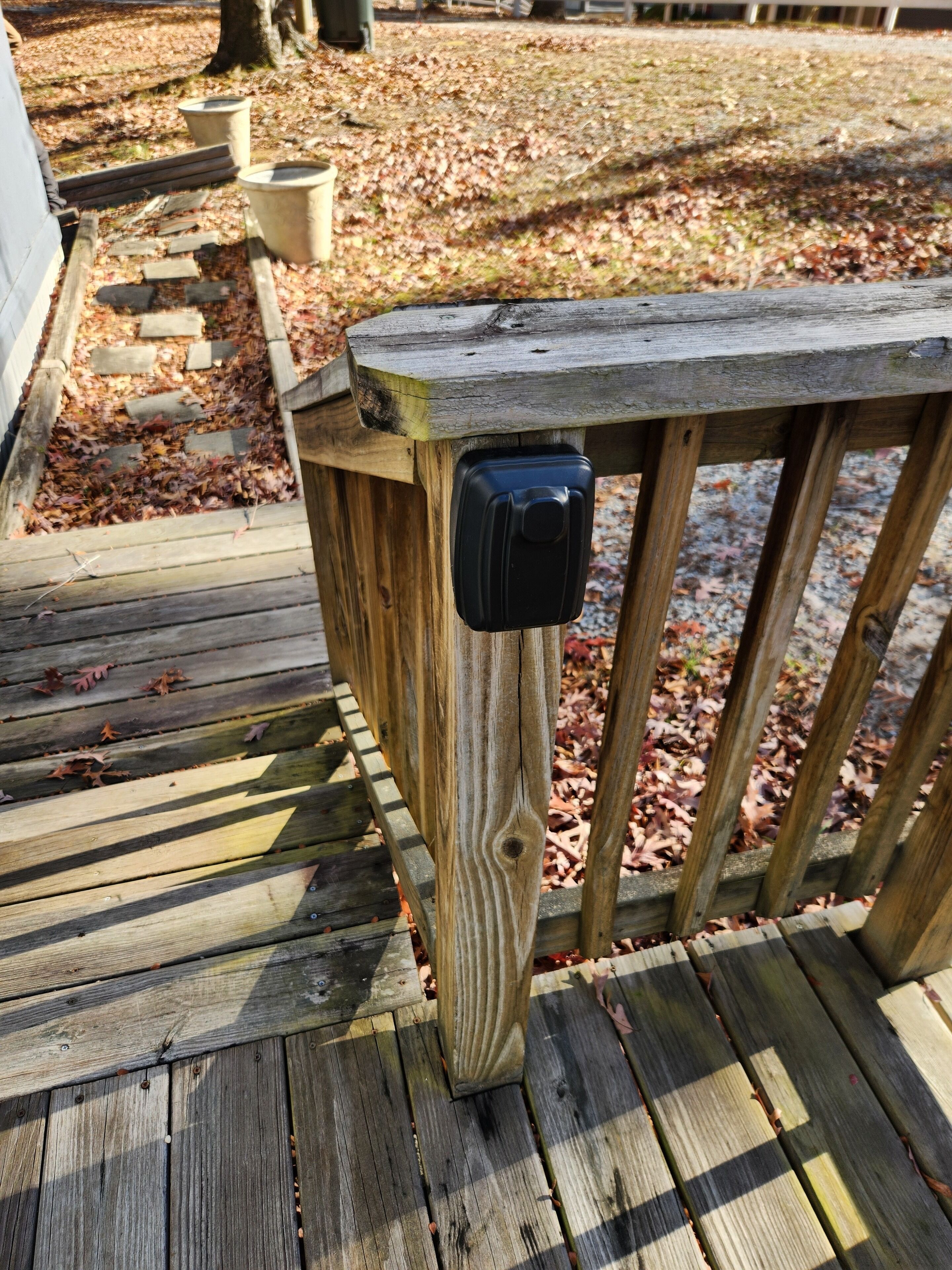 Une terrasse en bois avec une rambarde en métal et un objet noir fixé à celle-ci.