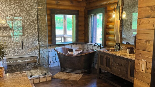 Une salle de bain rustique avec une baignoire sur pieds, des murs en bois et un pare-baignoire en pierre.
