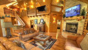 L’intérieur d’une cabane en rondins, avec un escalier en bois, des canapés en cuir, une cheminée et un téléviseur fixé au mur.