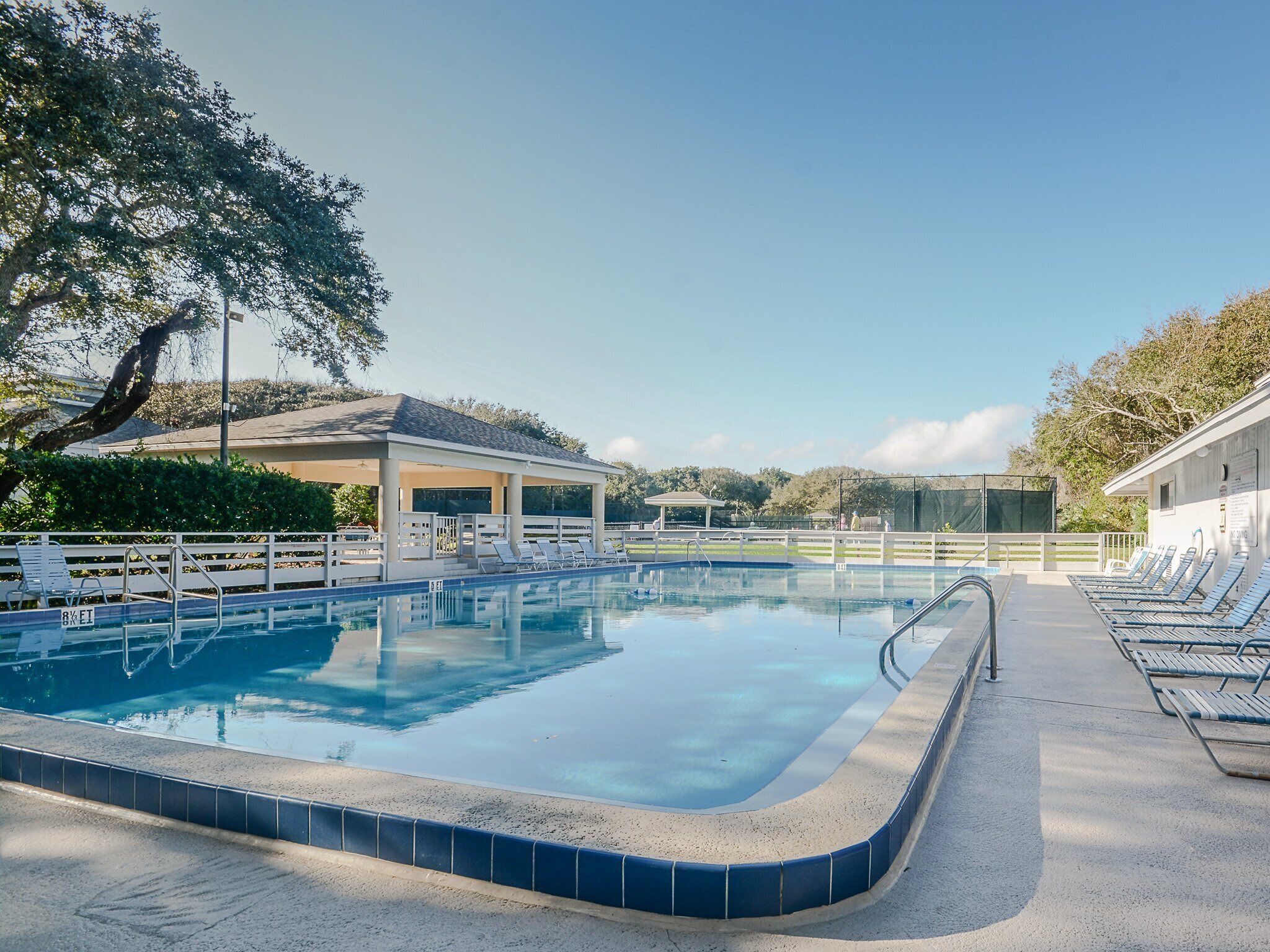 Piscina com borda azulejada, espreguiçadeiras e um pavilhão coberto.