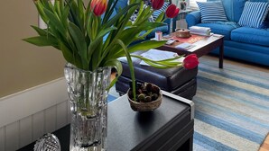 A living room with a blue sofa, a coffee table with papers, and a vase with flowers. - Direct Beach Access, Priv. Saltwater Pool,  Hottub, Elevator, BR 5; bath 5 (Kill Devil Hills)