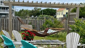 A patio area with turquoise Adirondack chairs, a wooden pergola, and a hammock. - Direct Beach Access, Priv. Saltwater Pool,  Hottub, Elevator, BR 5; bath 5 (Kill Devil Hills)