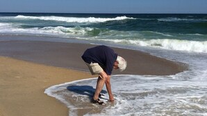 A person bending over on a sandy beach with waves in the background. - Direct Beach Access, Priv. Saltwater Pool,  Hottub, Elevator, BR 5; bath 5 (Kill Devil Hills)