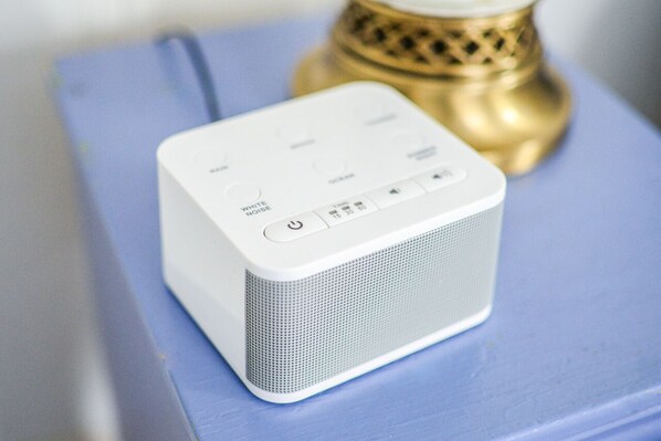 Un altavoz portátil blanco sobre una superficie azul, con un objeto dorado al fondo.