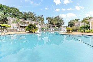 A swimming pool surrounded by buildings with balconies, trees, and a clear sky. - Beach Walk -optional BIKES-Pool-Walk 2 PierVillage (Saint Simons Island)