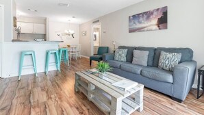 Una sala de estar moderna con un sofá gris, taburetes turquesa y una mesa de centro de madera.