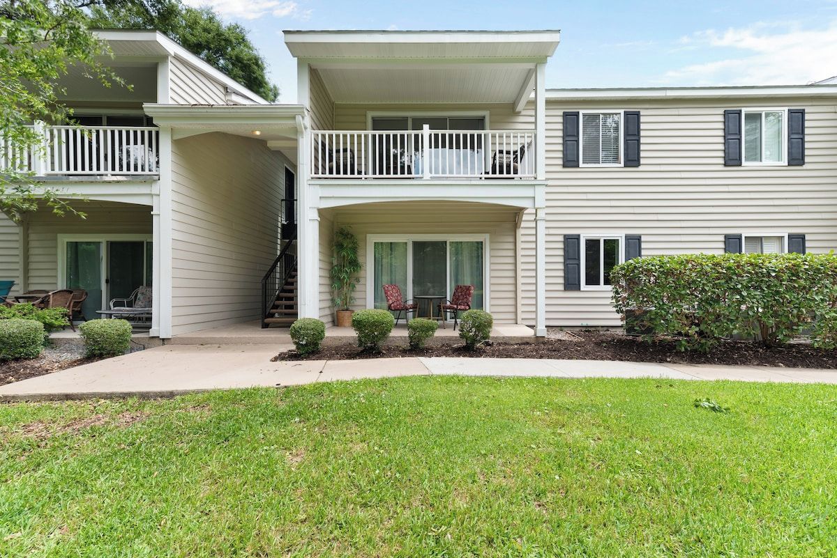 A two-story residential building with a covered front porch, a small garden, and a visible staircase leading to the upper floor.