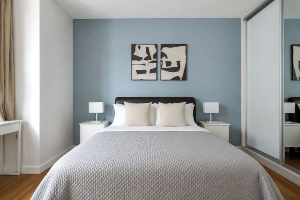 A bedroom with a bed, two bedside tables, a nightstand, and a mirror.