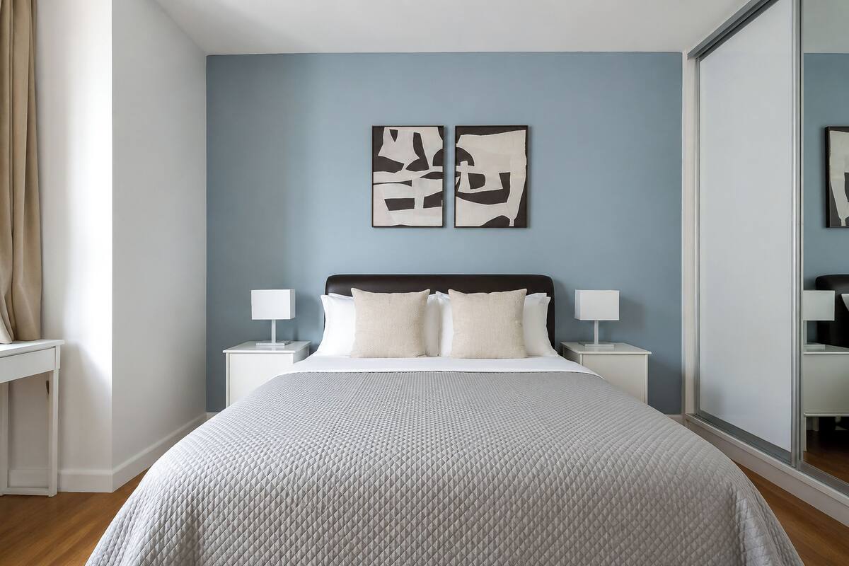 Ein Schlafzimmer mit einem Bett, zwei Nachttischen, einem Schminktisch und abstrakter Wandkunst.