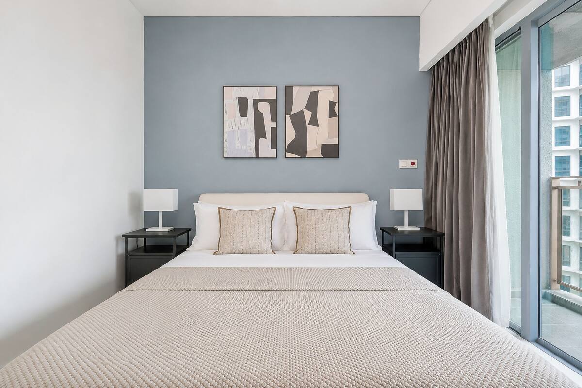 Ein Hotelzimmer mit einem großen Bett, zwei Nachttischen, einem Fenster mit Vorhängen und abstrakter Wandkunst.