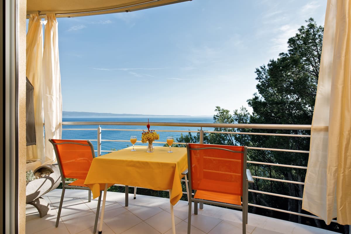 A balcony with a yellow table and orange chairs, overlooking a scenic view of the sea and distant land.
