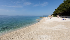 A beach with clear water, pebbly shore, and a few people sunbathing. - Ark Beach Hotel (Split)